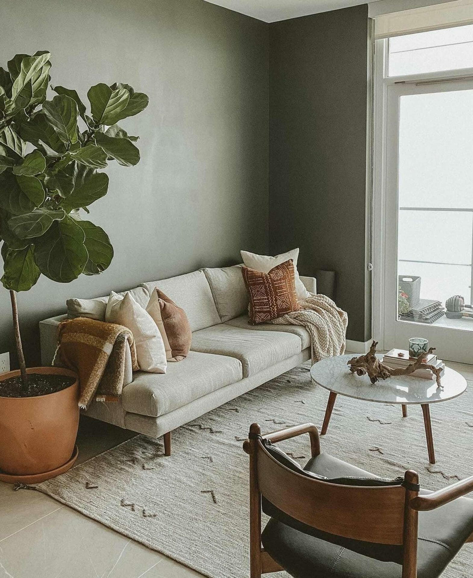 Blogger Travis Collins' minimalist living room features a light sofa, fiddle leaf fig, leather chair, and marble coffee table.