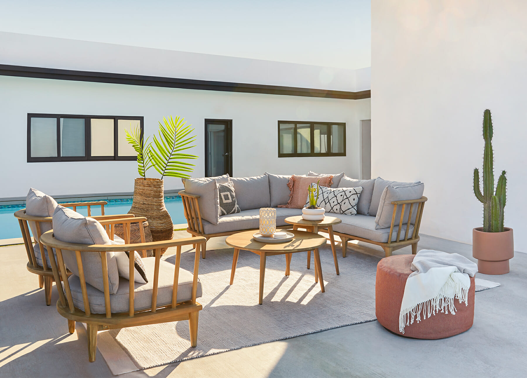 An outdoor sofa set is shown with a rug, cactus, and ottoman.
